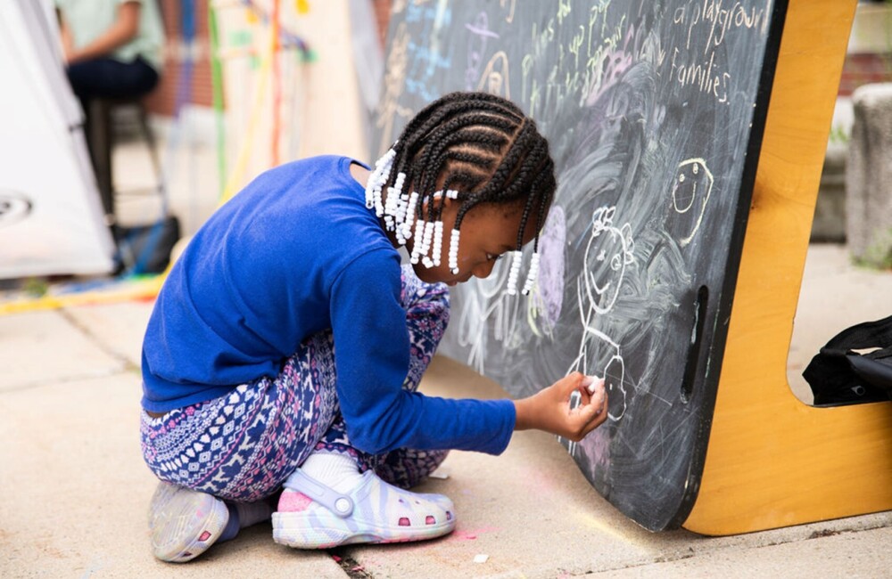 A young girl adds a drawing to a community chalk board