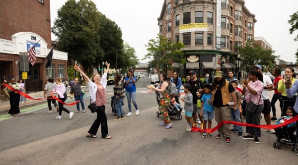 A woman raises her arms in the air after cutting the ribbon to unveil the new mural. Behind her, a crowd claps and celebrates.