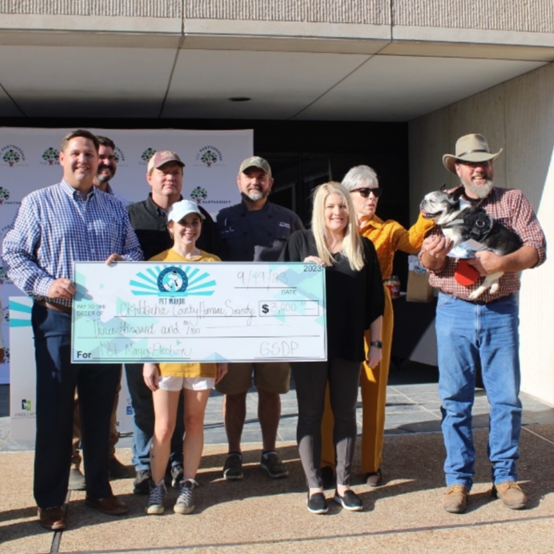 A group of people holding a large award check; one of the men is holding a dog