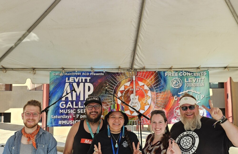 Five people pose for picture in tent in front of event poster.