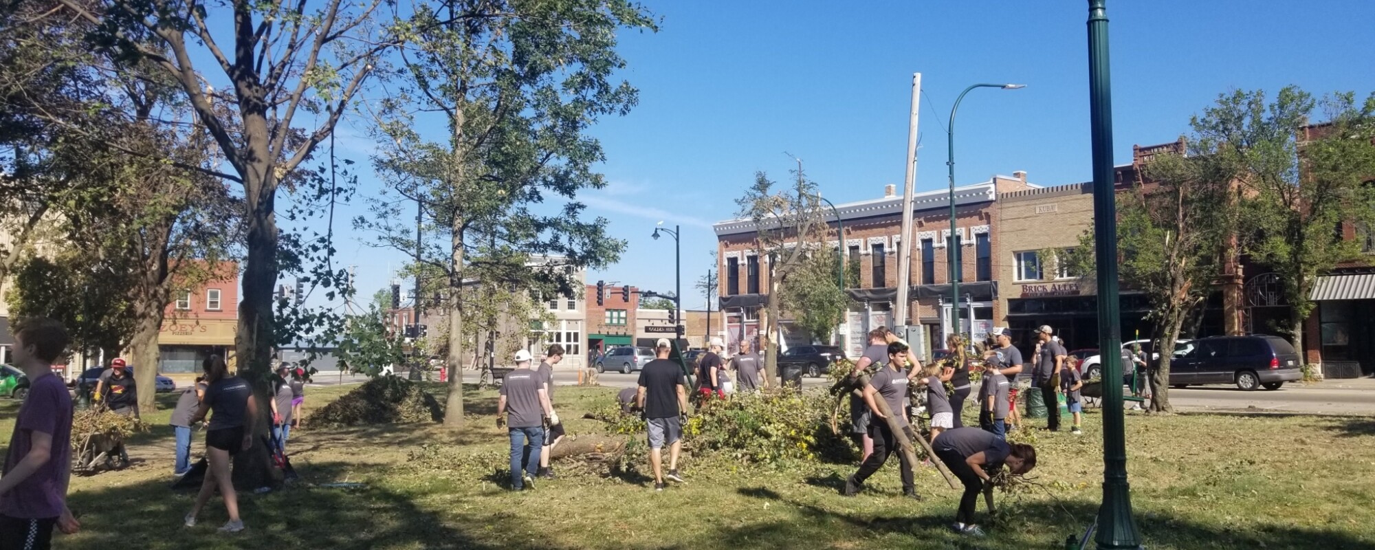 People picking up fallen tree limbs and other debris in a downtown park