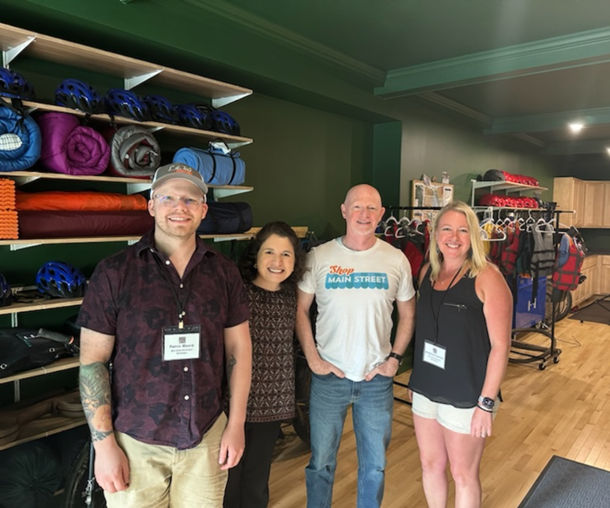 Four people pose in front of a wall of outdoor gear