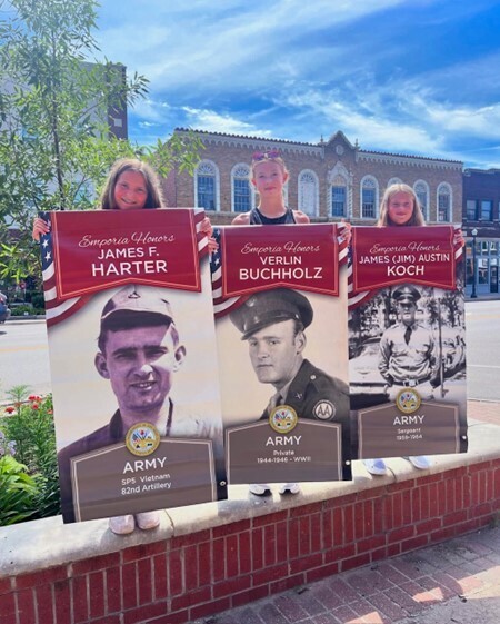 Three girls holding up banners featuring veterans from their community