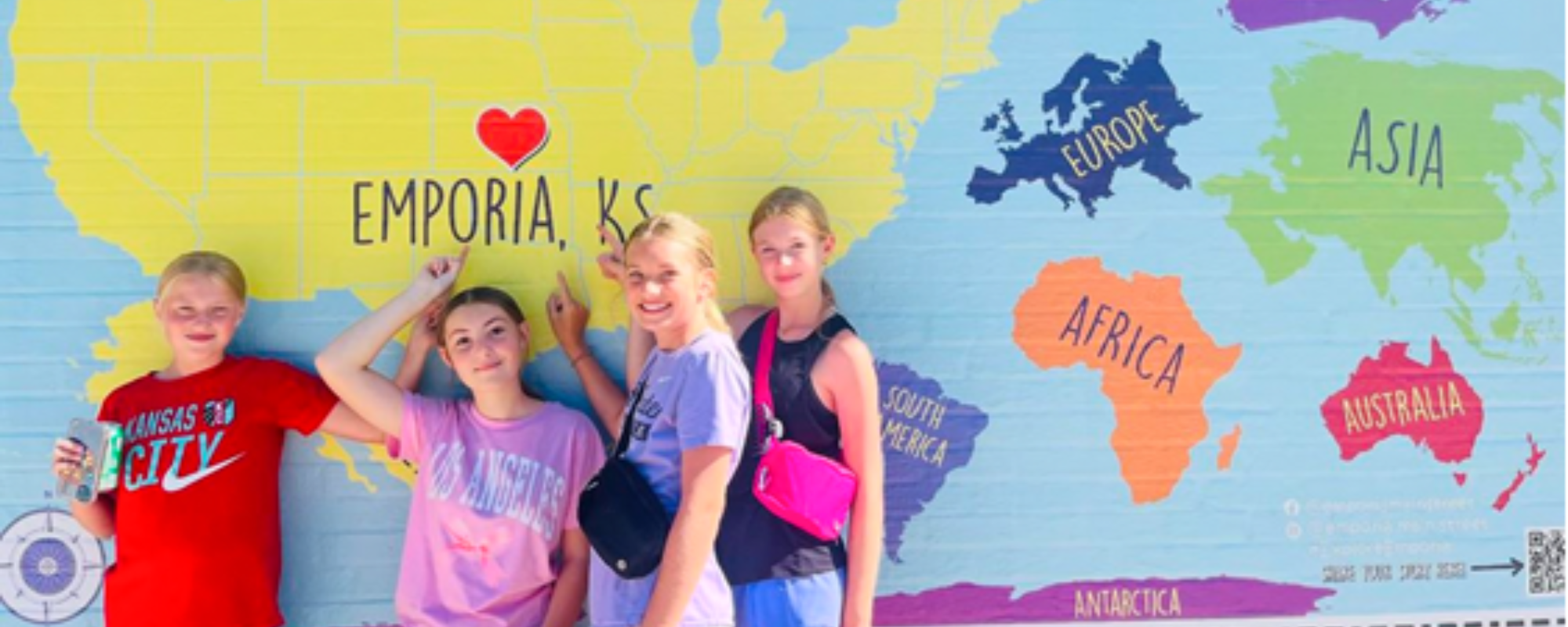 Four pre-teen girls post in front of a downtown mural featuring a map of the US