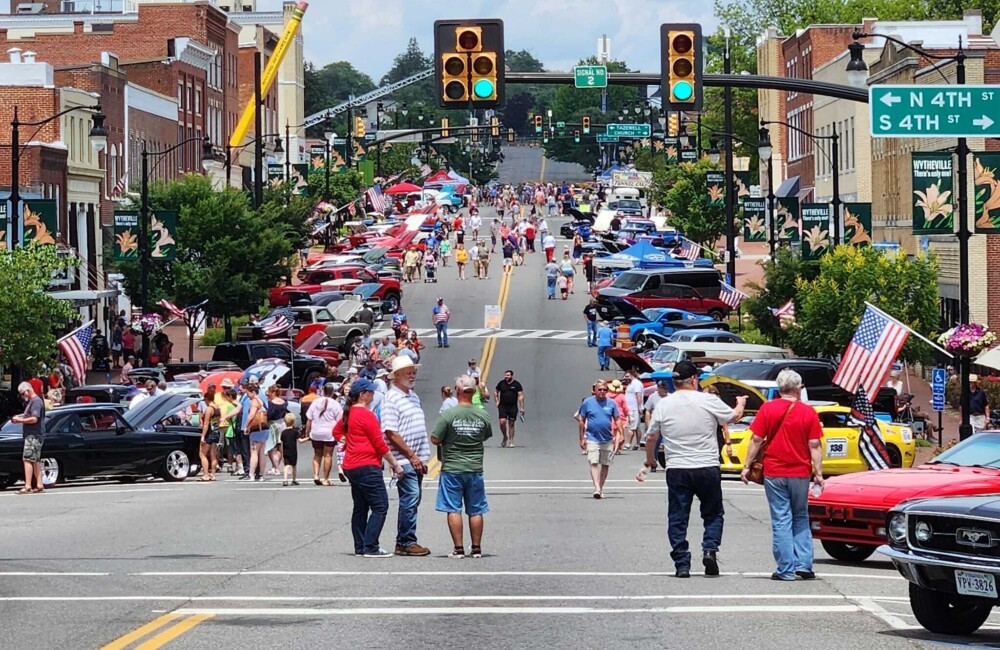 People stroll down a wide street lined with classic cars.