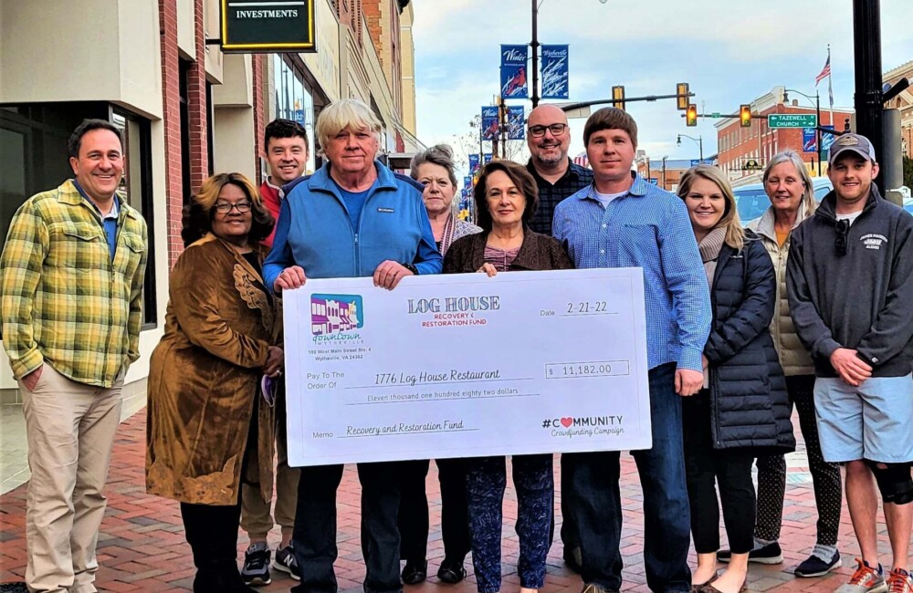 A small group of people gather on a sidewalk for a photo with a large ceremonial check.