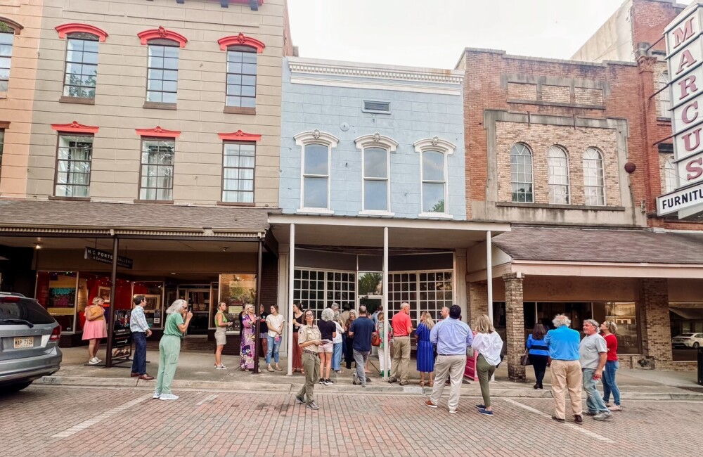 A large group of people gather in front of vacant storefronts.