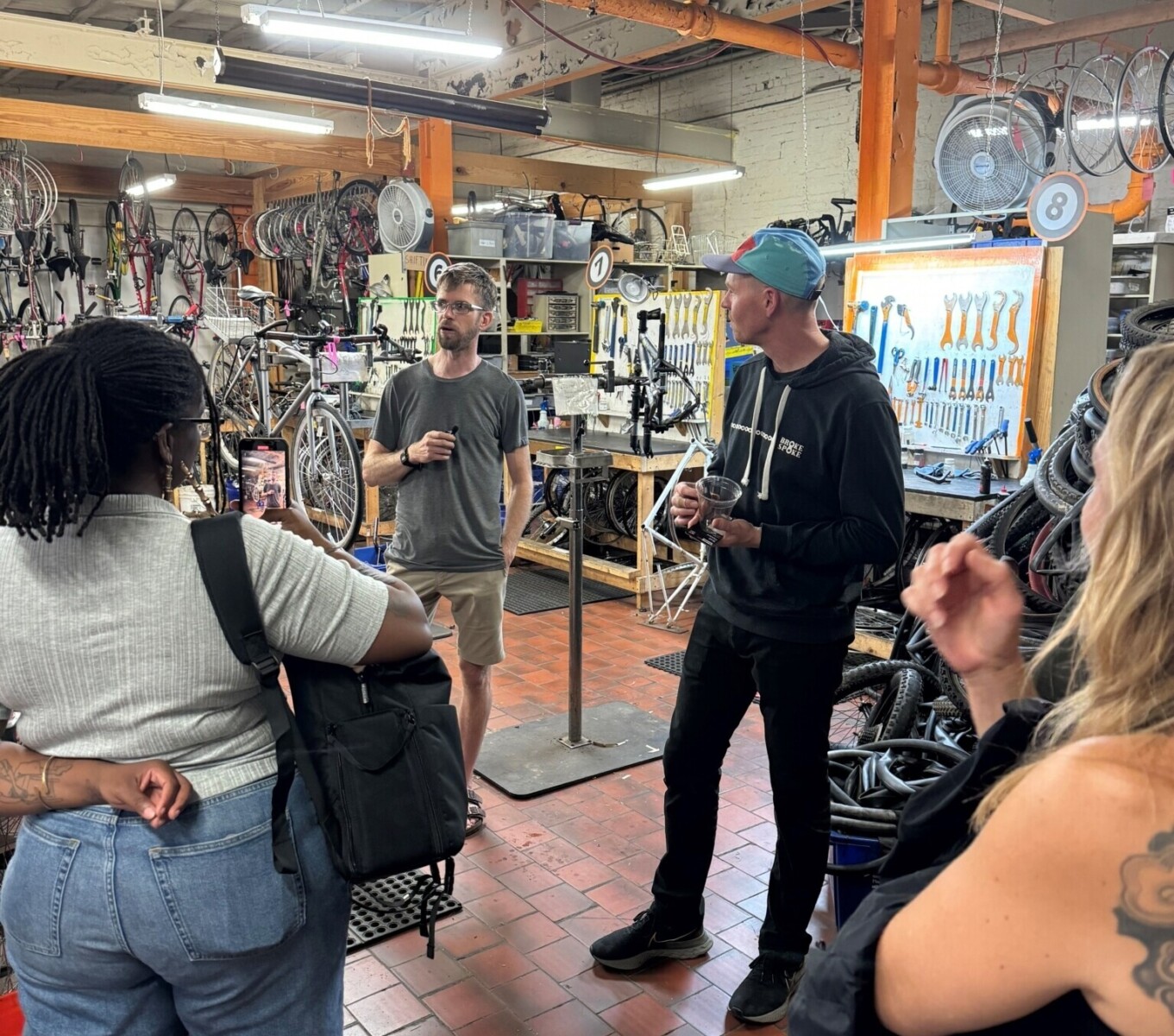 A group of people listens to two presenters sharing information in a bicycle repair shop