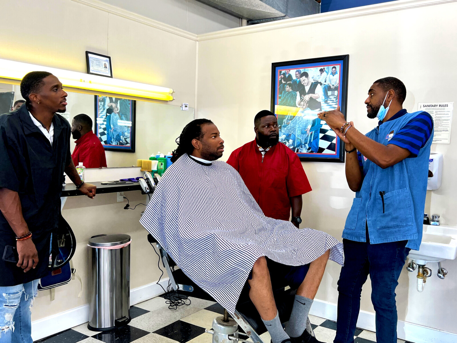 Four men in a Black barbershop having a conversation around the barber chair