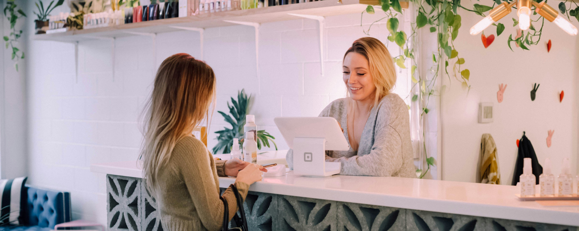 A woman using a tablet point of sale system helps check out a customer at the counter in a small business