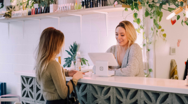 A woman using a tablet point of sale system helps check out a customer at the counter in a small business