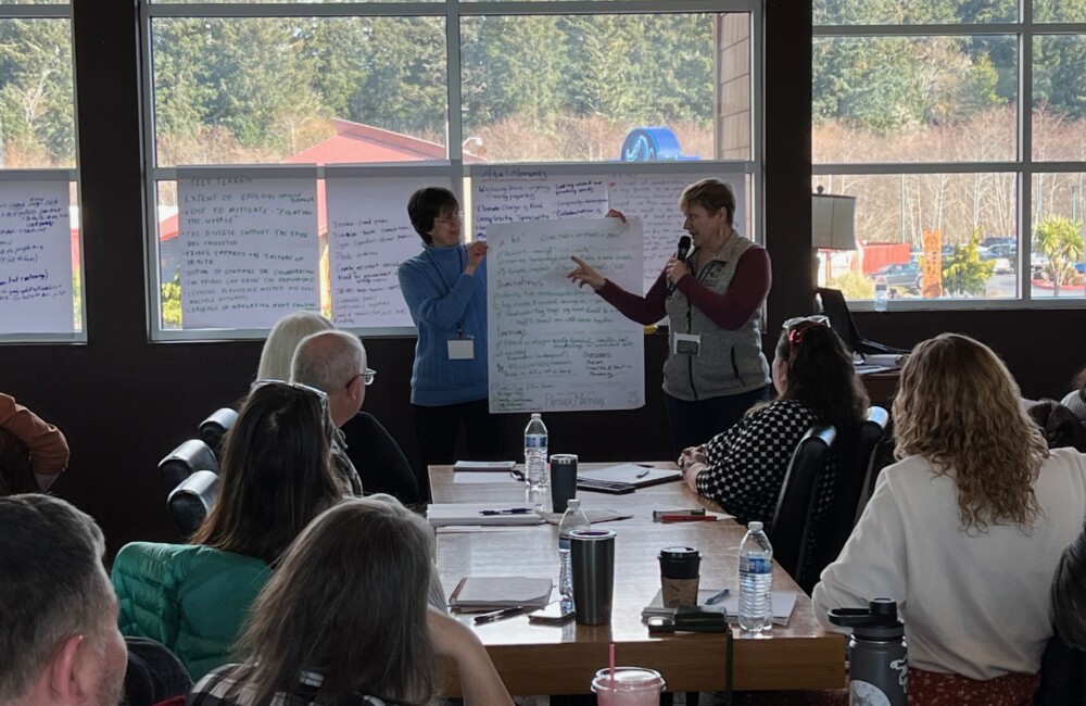 Two speakers lead a discussion in front of large notepad in conference room.