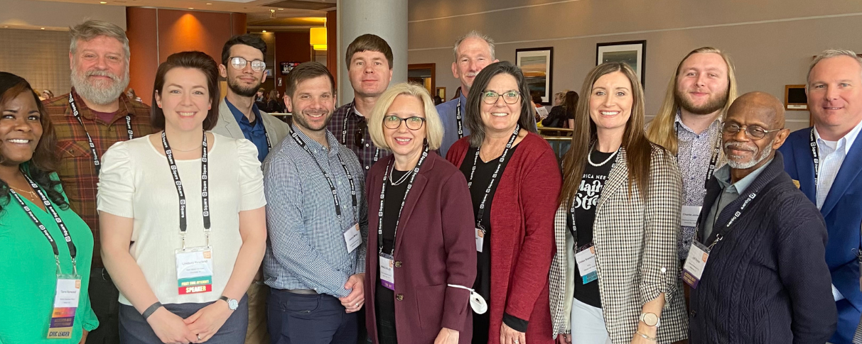 A group of 14 people pose for a photo at a conference.