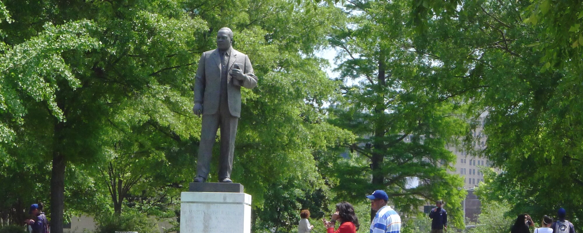 People stroll through a beautifully landscaped park while a man and woman pause to visit a bronze statue of Martin Luther King, Jr.