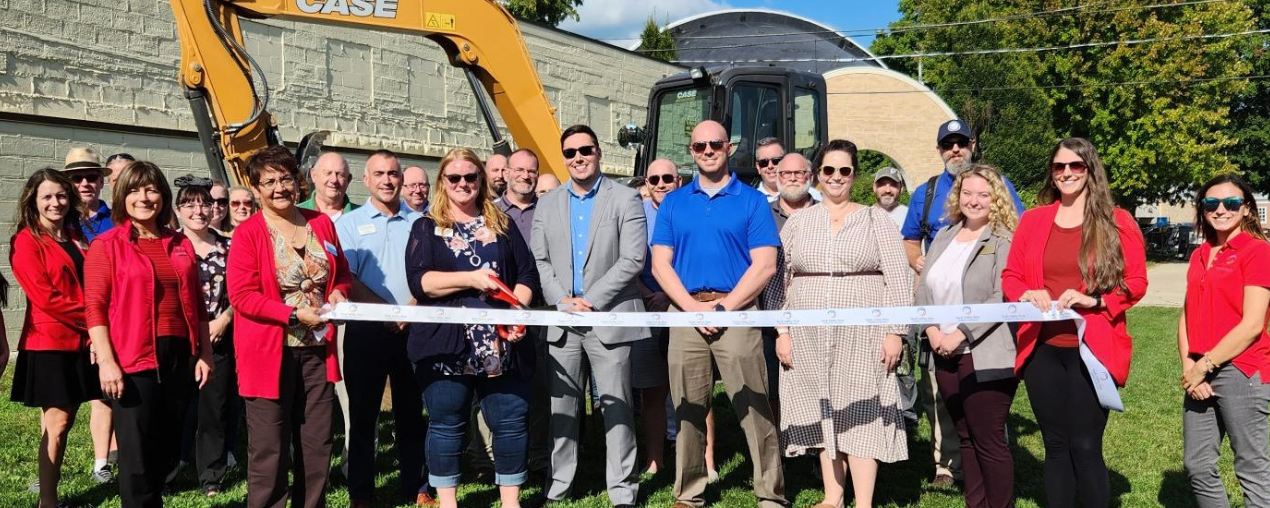 People standing in front of an excavator for a groundbreaking ceremony