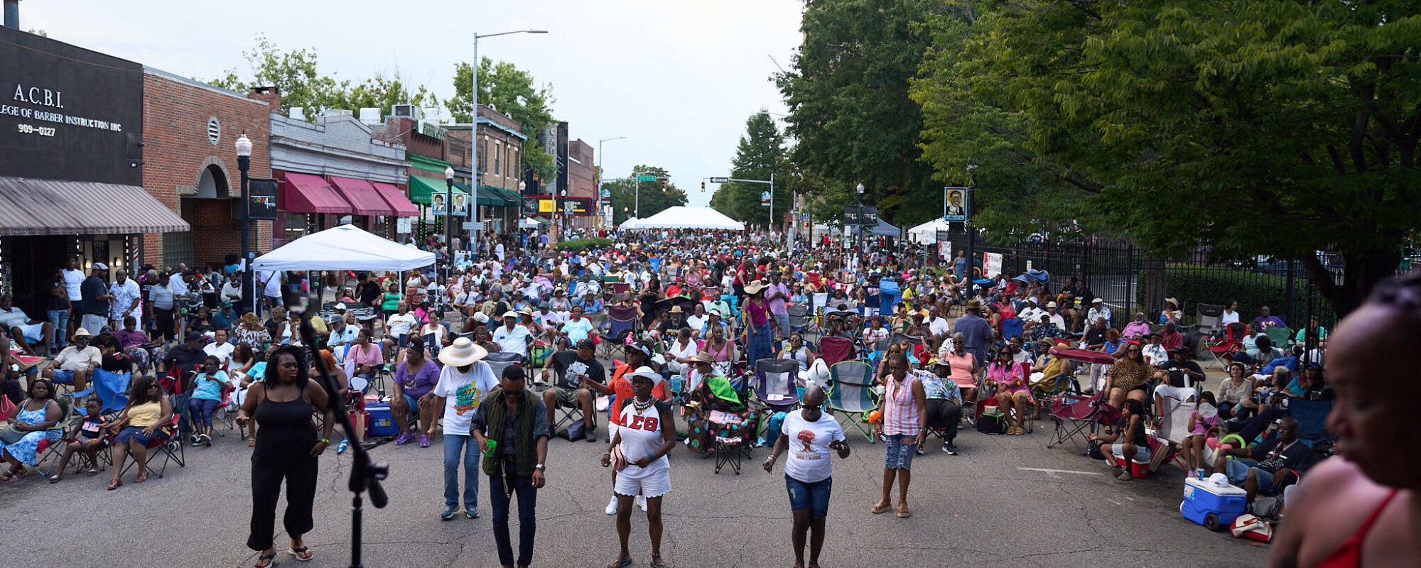 Street lined with storefronts and filled with people enjoying a concert.