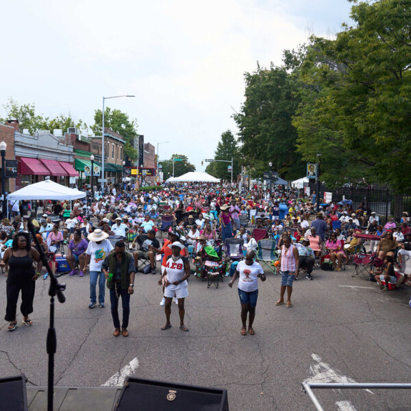 Street lined with storefronts and filled with people enjoying a concert.