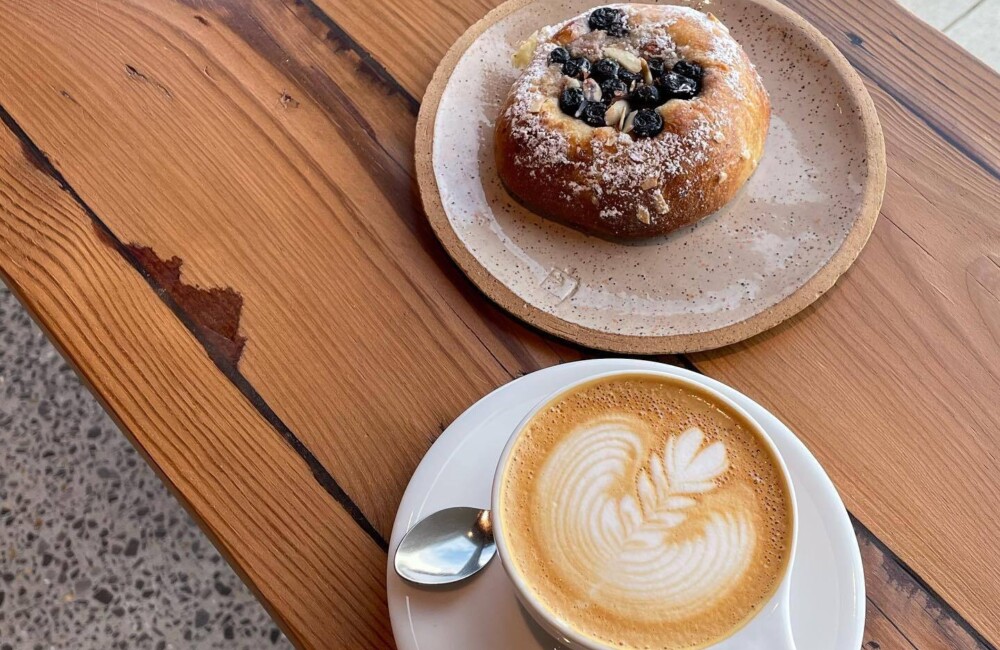 A latte and pastry served on simple plates rest on a wooden table.