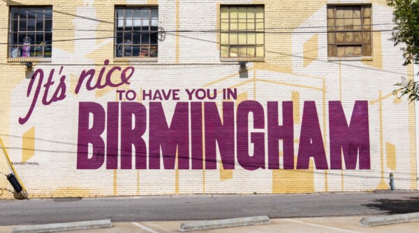 Mural en la pared exterior de un edificio en el que se lee "It's Nice to Have you in Birmingham" ("Es bueno tenerte en Birmingham") en un intenso color magenta.