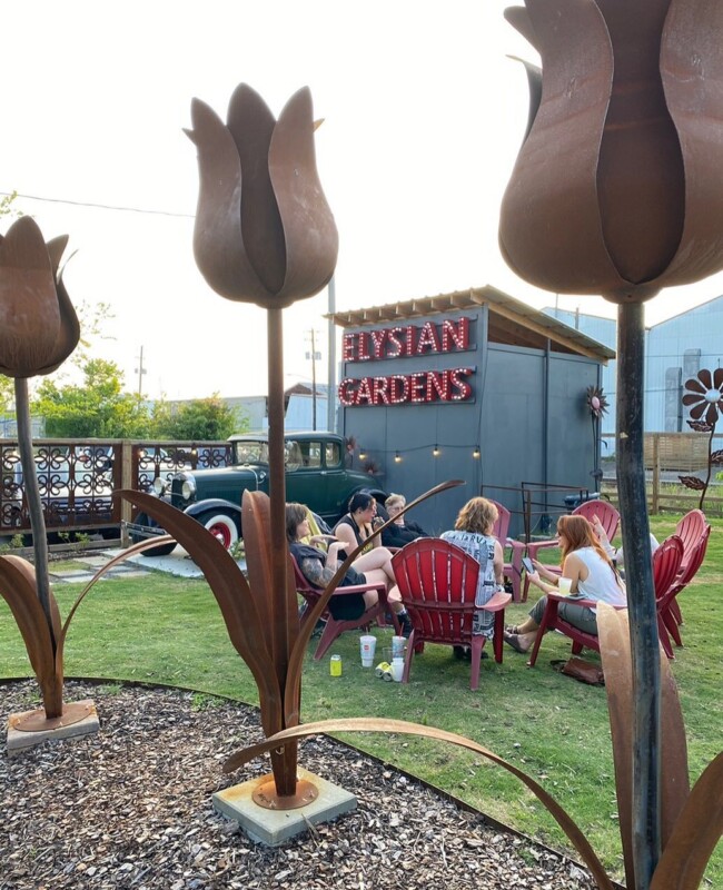 Large metal tulip sculptures in the foreground and a group of people sitting in red lawn chairs on a grassy area in the background.