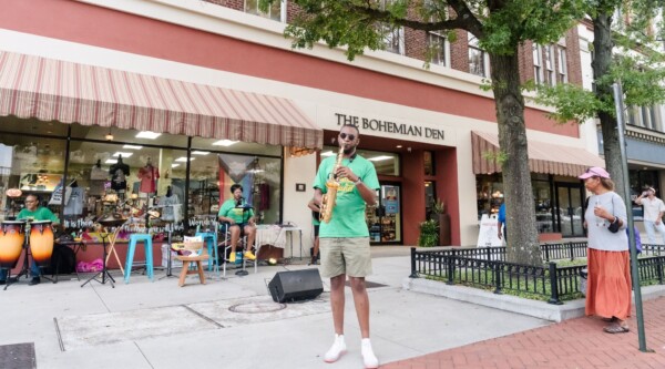 Un saxofonista, un batería y un vocalista instalados en una amplia acera actúan para los peatones.