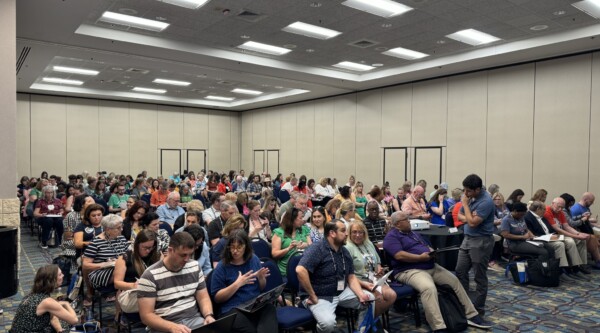 Conference session room filled with people chatting before the presentation begins.