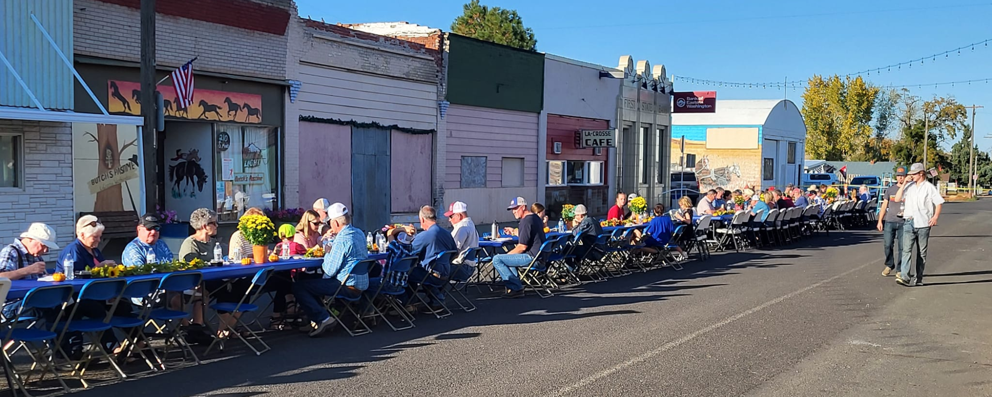 People sit at a long table on the street in a historic downtown