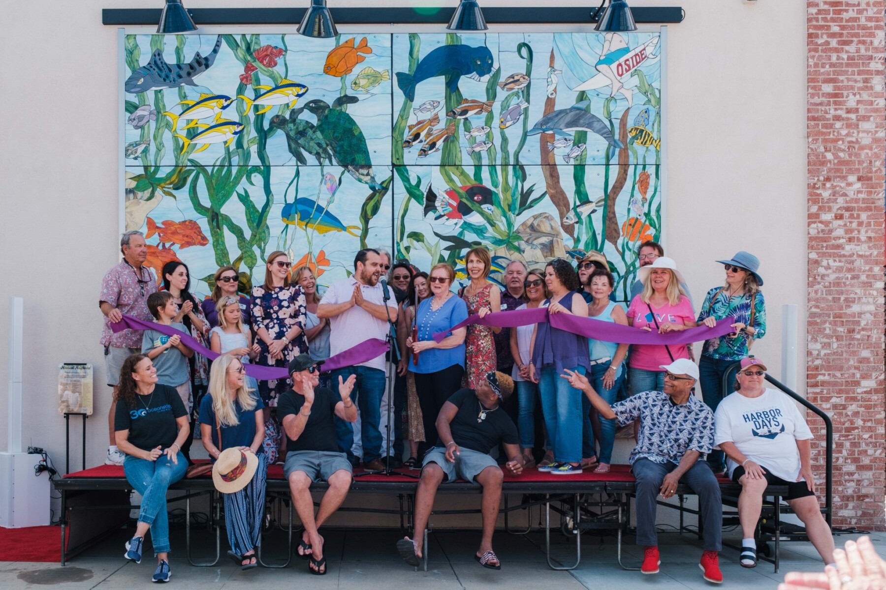 People pose during a ribbon cutting for a stained glass mural featuring sea creatures