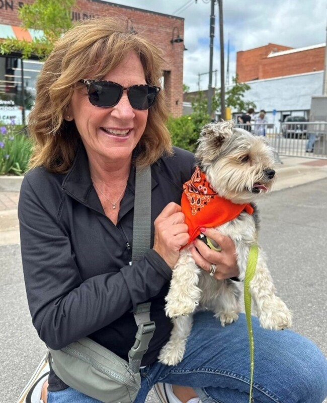 A woman holding a dog wearing an orange bandana