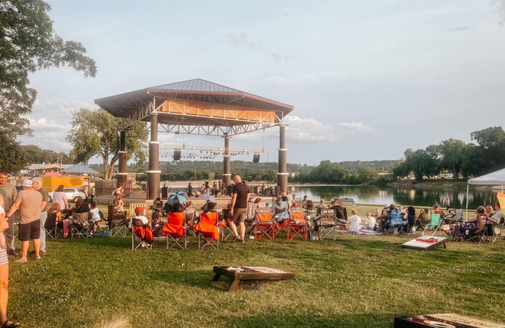 People sit in lawn chairs in front of outdoor stage on sunny day.