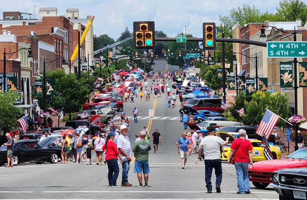 People stroll down a wide street lined with classic cars.