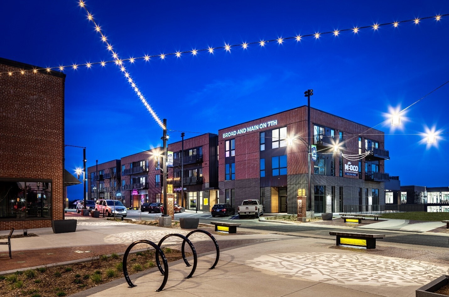 Downtown streetscape with a pocket park, bike racks, benches, and decorative overhead lighting