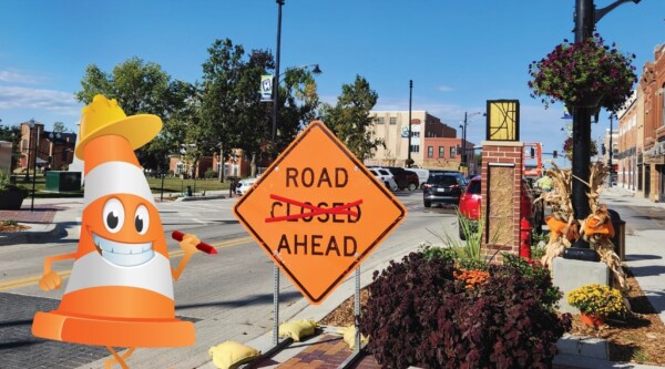 Photo of a downtown street with construction signs and a cartoon traffic cone