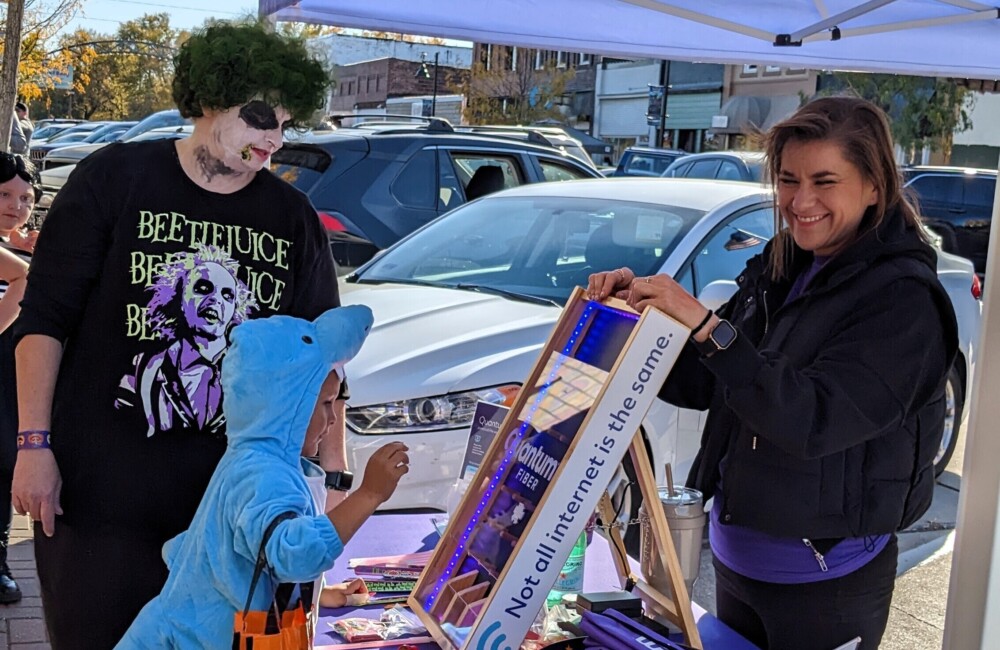 A kid dressed like a dinosaur and a man wearing a beetlejuice costume play a small game at a tent in the downtown