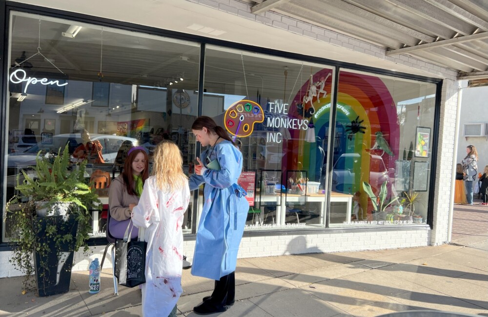 Two people on costumes take Halloween candy from a trick or treat stand outside a small business