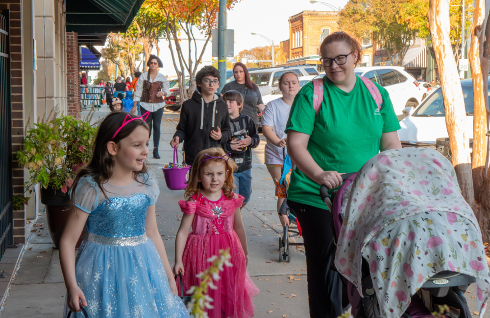 Trick or treaters in costume walk down a sidewalk