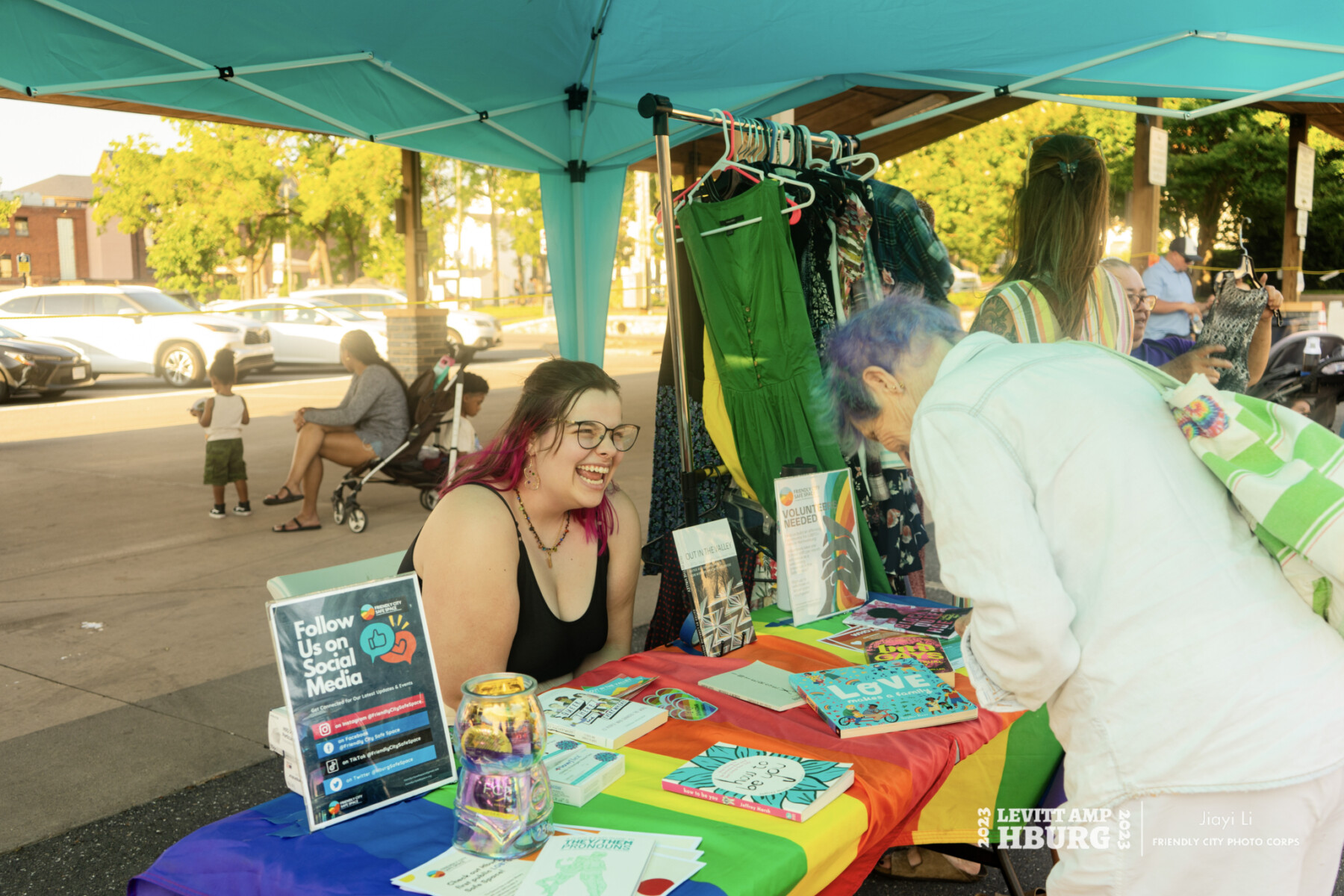 Woman sitting at vendor table smiles at woman looking at items on table.