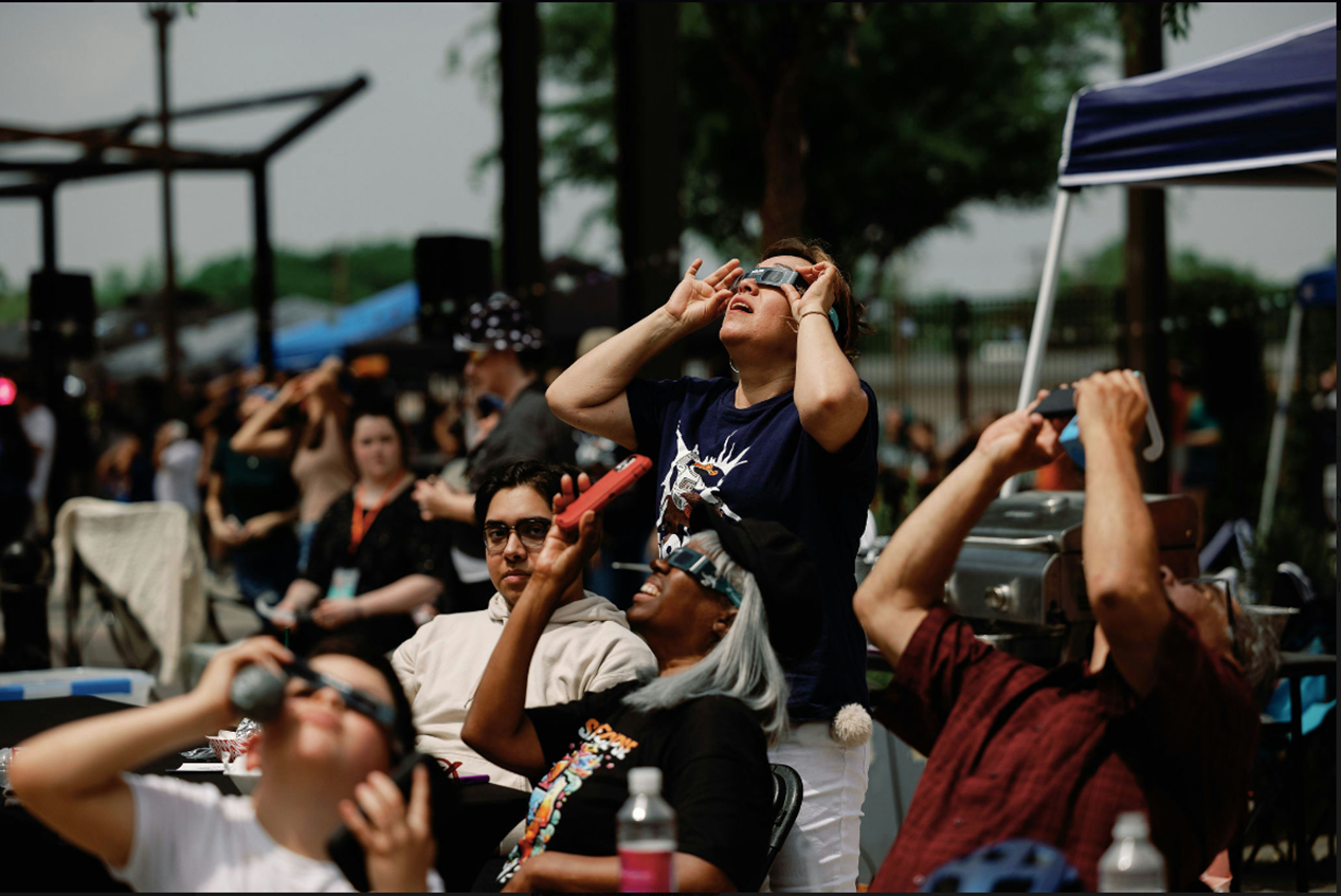 People look up at the sky through eclipse glasses