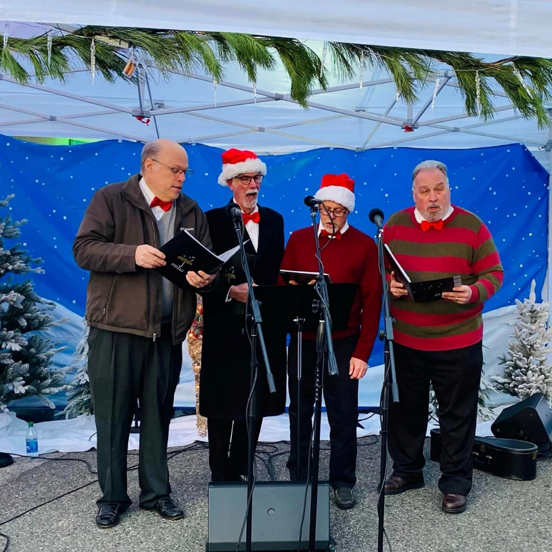 Four men on a stage performing carols