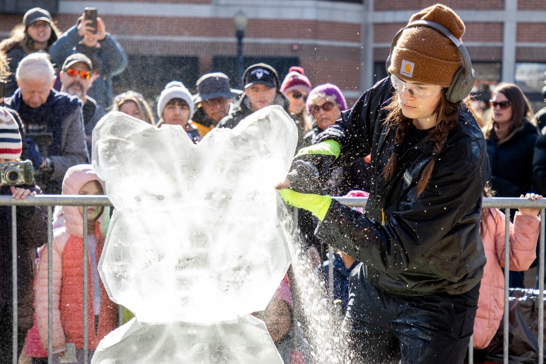 A woman with a chainsaw carves a block of ice into a sculpture