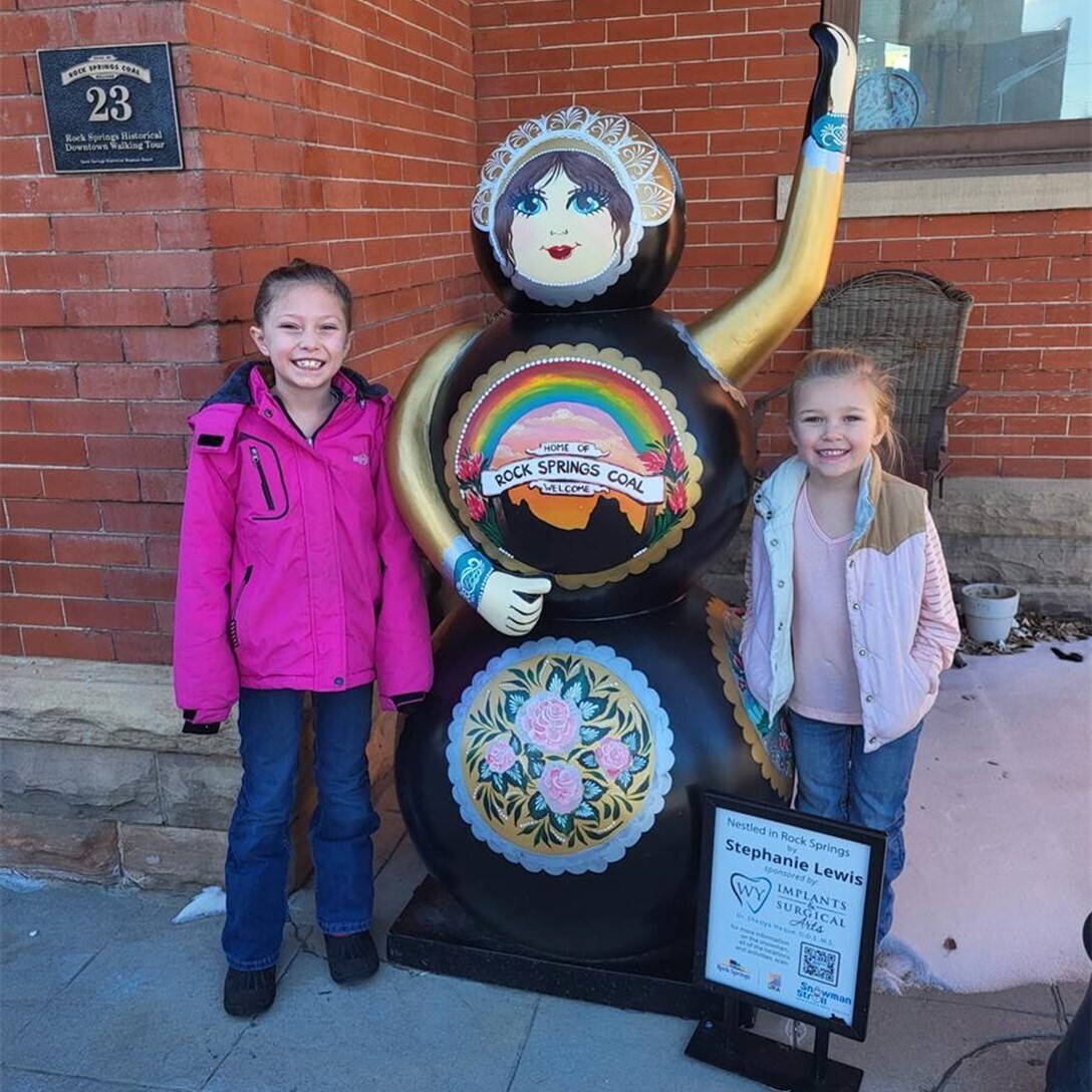 Two young girls pose next to a fiberglass snowman painted with unique art