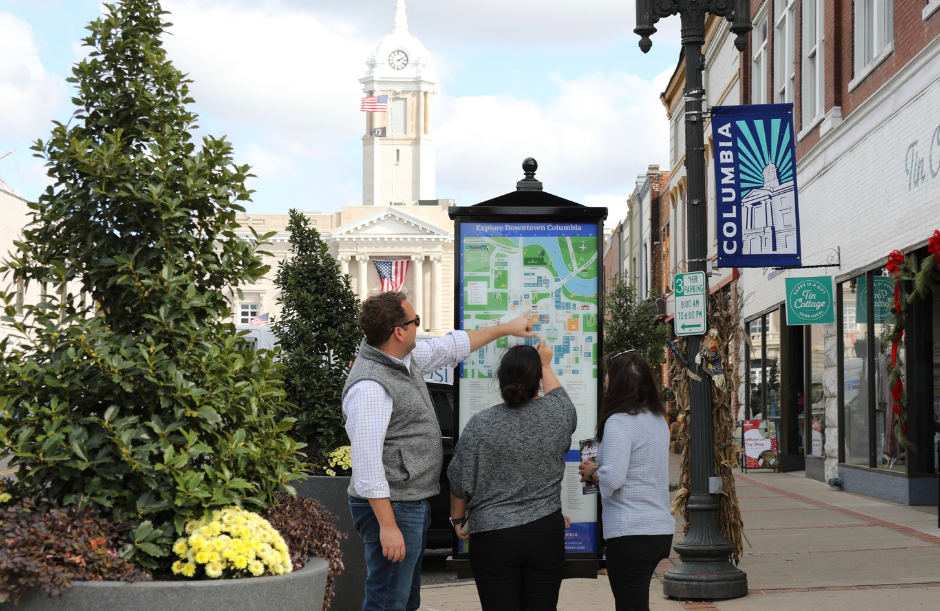 Three people gather around an informational kiosk in a downtown area