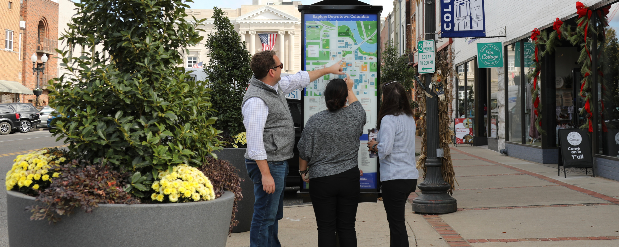 Three people gather around an informational kiosk in a downtown area