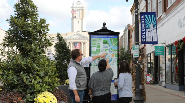 Three people gather around an informational kiosk in a downtown area