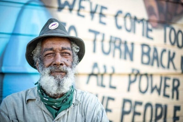 An elderly man stands in front of a mural