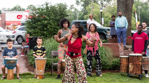 A woman dances while children play drums at a musical celebration