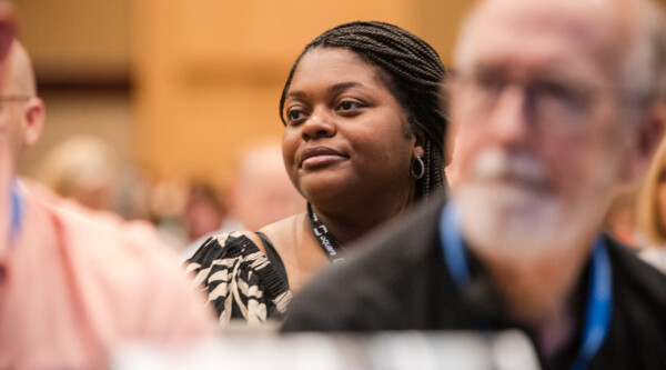 People listen intently to a speaker; in the center and in focus is a woman smiling.