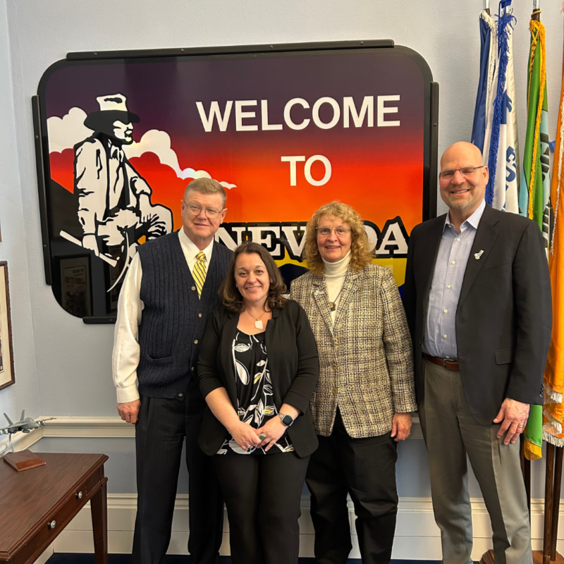 Four people posing in front of a sign that says "Welcome to Nevada" with a drawing of a cowboy