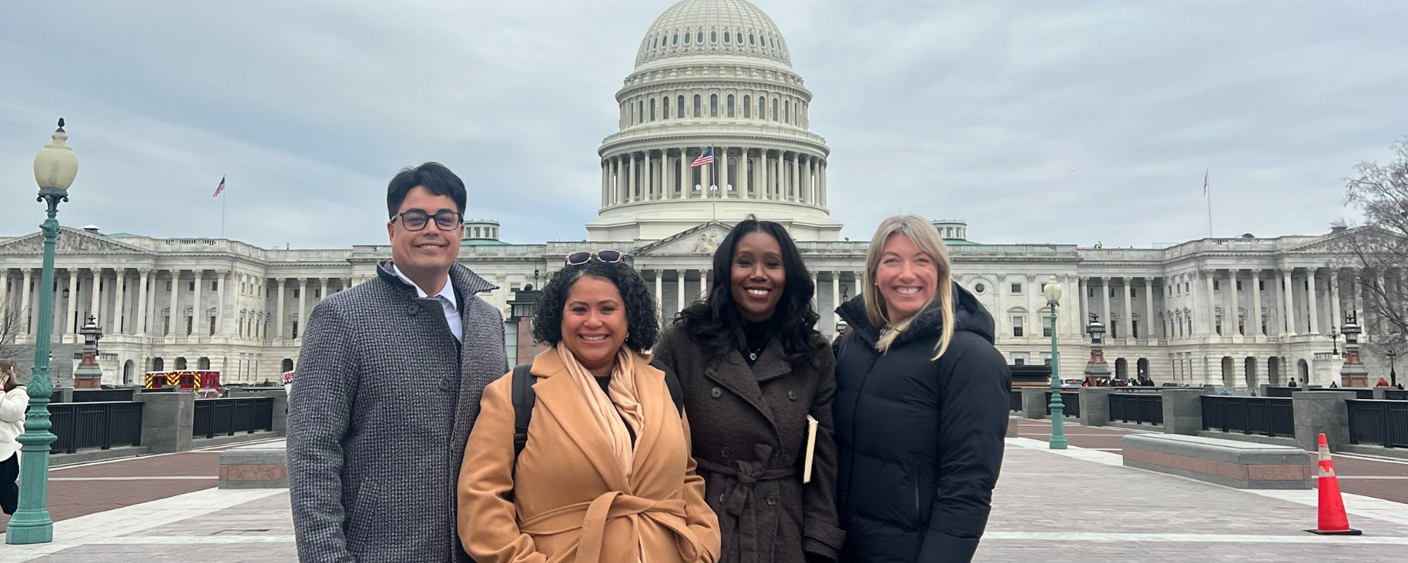 Four people posing for a photo in front of the Capitol building