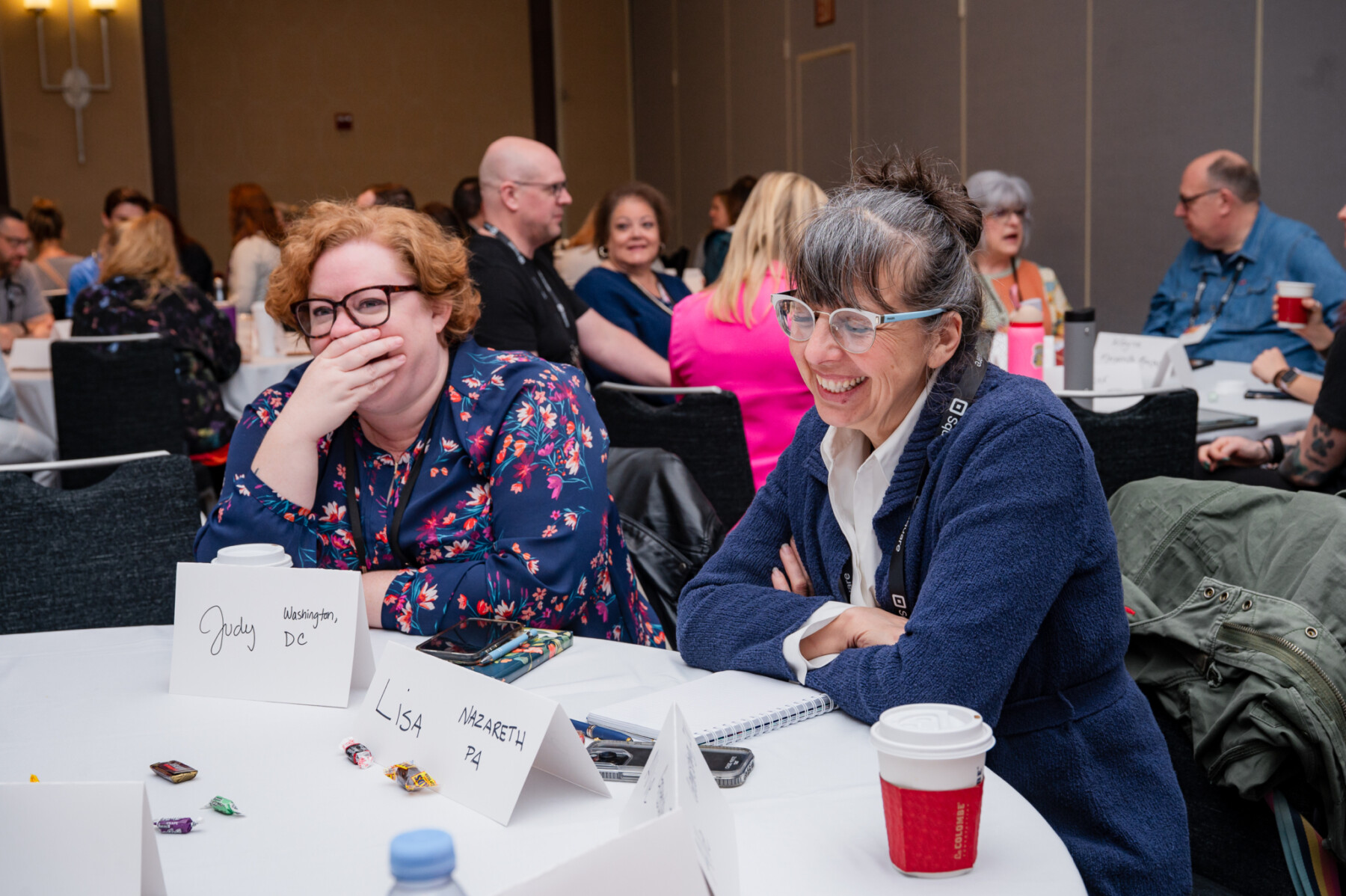 Two women sitting at a table laugh during a conference session